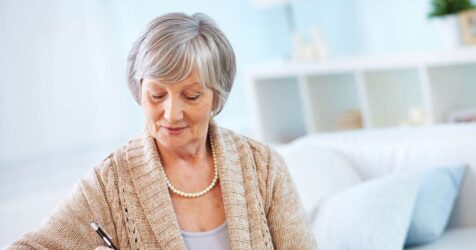 An elderly woman, engaged in her senior living search, is writing on a piece of paper.