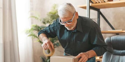 An older man is downsizing by putting tape on a box.