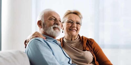 An elderly couple downsizing to senior living, sitting on a couch.