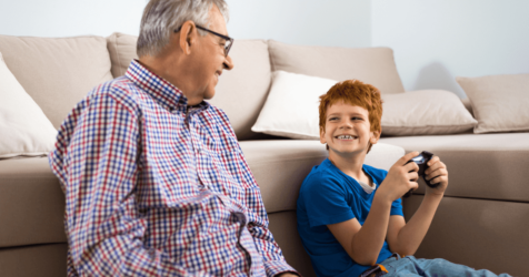 Older man sitting on the floor playing video games with his grandson