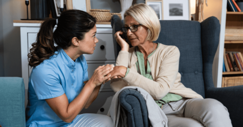 A nurse is engaging in conversation with an older woman in a chair, discussing at-home care.